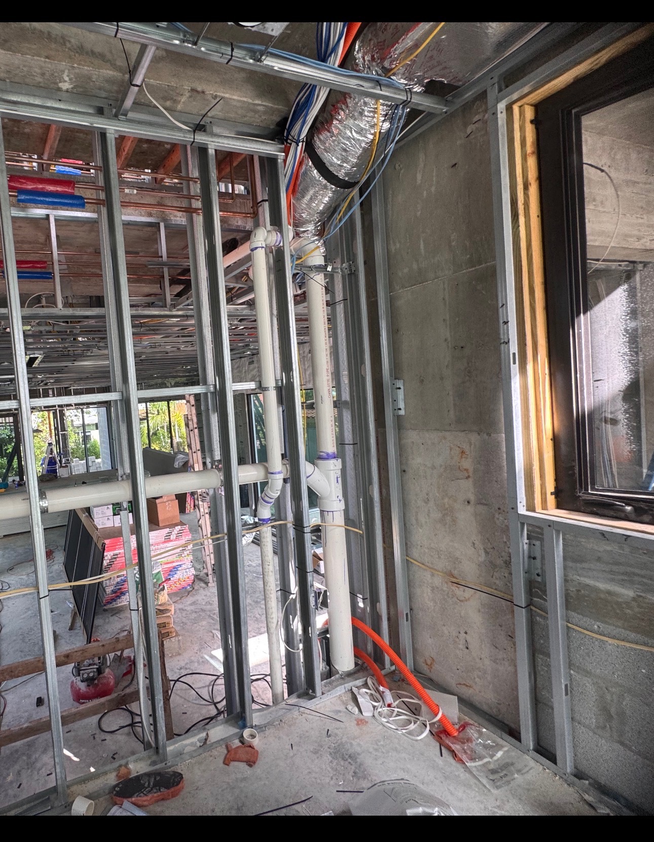 Steel-stud framing with vertical PVC stacks and overhead HVAC duct in the conflict zone before resolution.